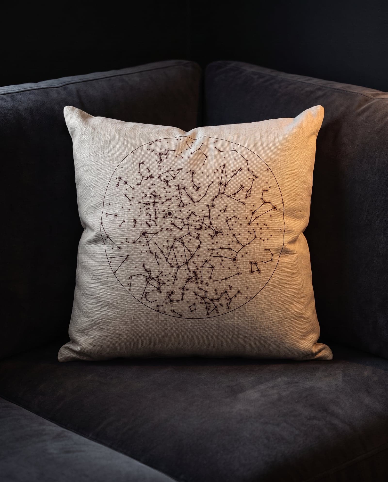 A cushion printed with a star chart, in the corner of a dark velvet sofa